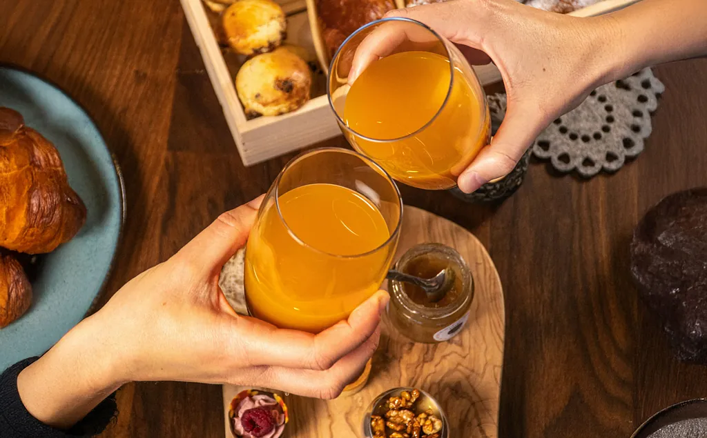 Zwei Hände mit Orangengläser, die sich zuprosten über Gebäck.